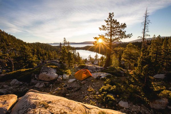 beautiful-shot-orange-tent-rocky-mountain-surrounded-by-trees-sunset