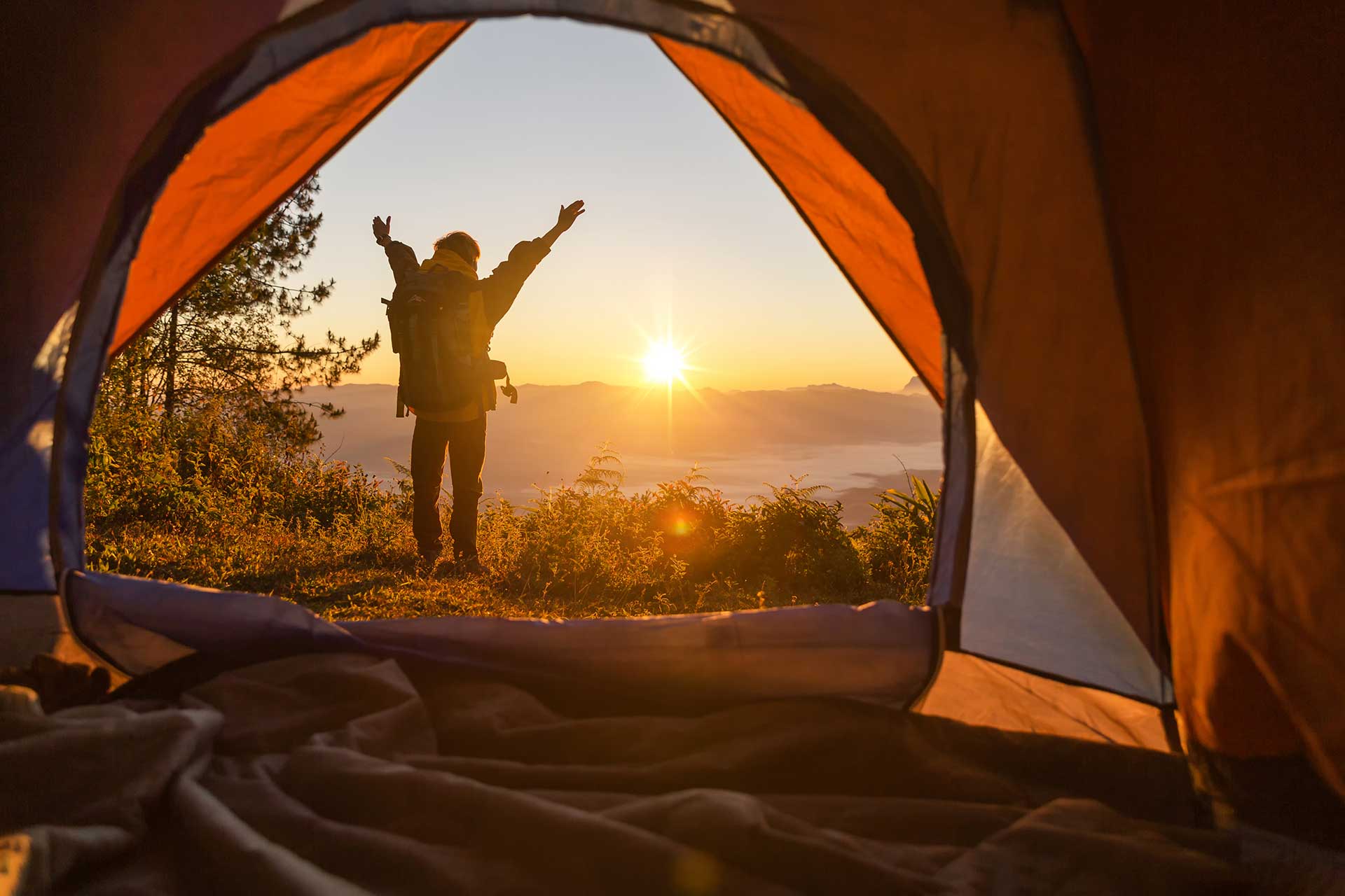 hiker-stand-camping-front-orange-tent-backpack-mountains